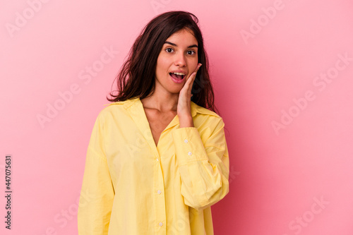Young caucasian woman isolated on pink background shouts loud, keeps eyes opened and hands tense. © Asier