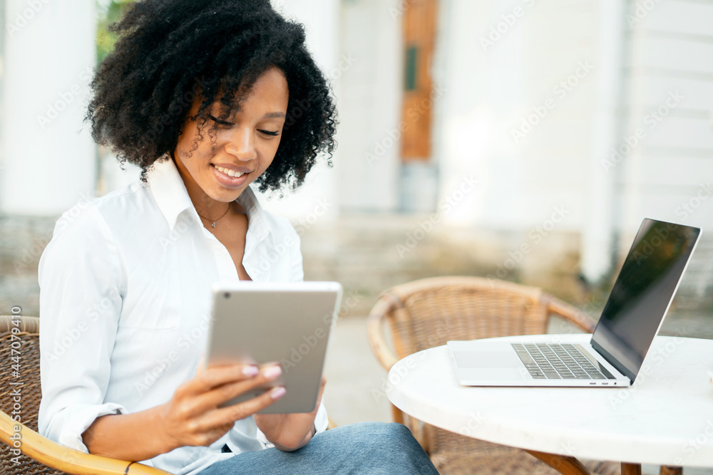 A student prints a message on a laptop on a social network to his subscribers. A woman of African-American appearance works on a computer. Curly hair and a white shirt.