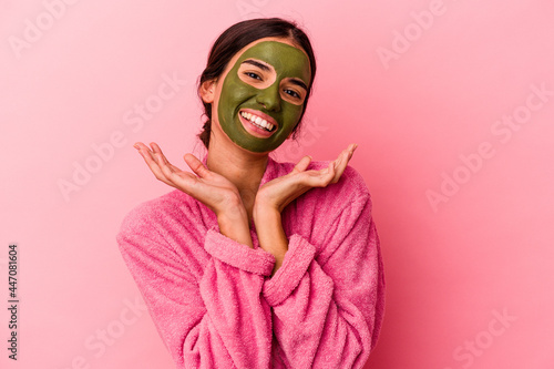 Young caucasian woman wearing a bathrobe and facial mask isolated on pink background