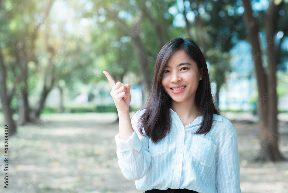 attractive adult business woman asian girl with happy and smile standing with finger pointing on walk way go to working between her office on morning under green forest. attractive adult business woman asian girl with happy and smile standing with finger pointing on walk way go to working between her office on morning under green forest.
