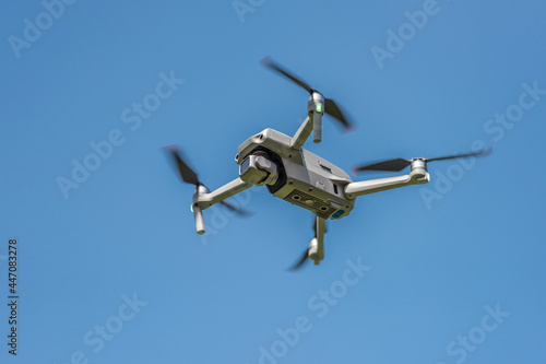 Flying drone with camera on a blue background with copy space. Airborne quadcopter. Also known as a drone or UAV, Unmanned Aerial Vehicle. Low angle view.