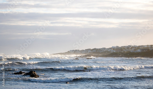 Ocean sunset view with vacation homes in the background and rocks and waves in the foreground.