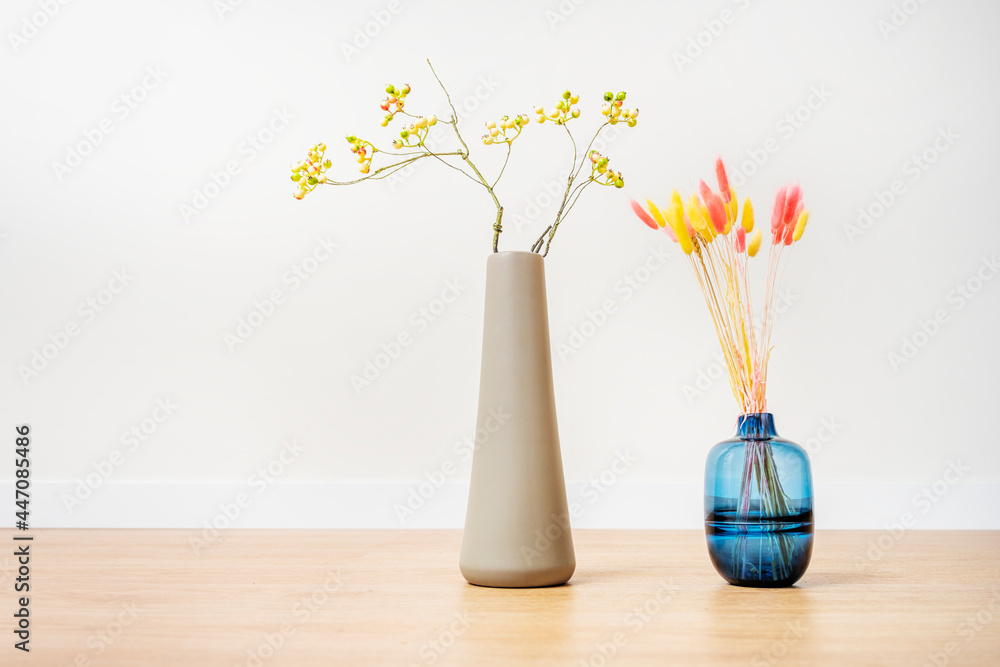 Obraz premium Decorative vases with colorful dried flower branches and yellow dried blueberries branches on oak floor and white background