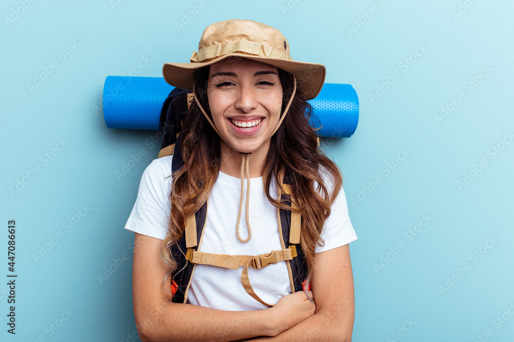 Young hiker mixed race woman isolated on blue background laughing and having fun. Young hiker mixed race woman isolated on blue background laughing and having fun.
