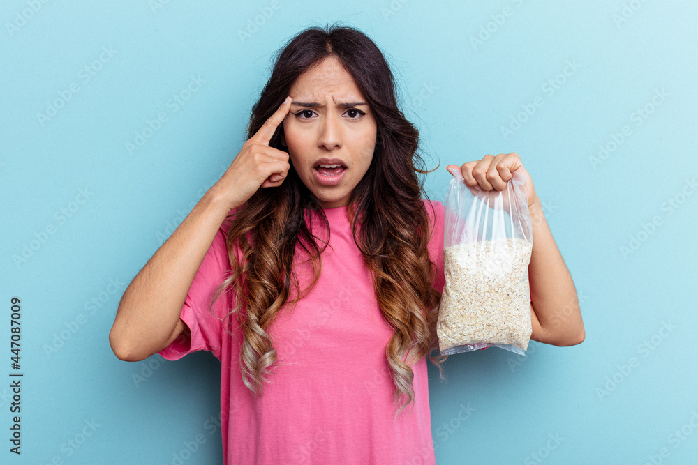Young mixed race woman holding oatmeal isolated on blue background showing a disappointment gesture with forefinger. Young mixed race woman holding oatmeal isolated on blue background showing a disappointment gesture with forefinger.