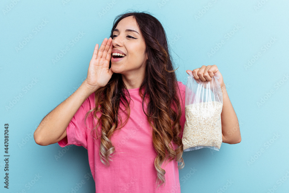 Young mixed race woman holding oatmeal isolated on blue background shouting and holding palm near opened mouth. Young mixed race woman holding oatmeal isolated on blue background shouting and holding palm near opened mouth.