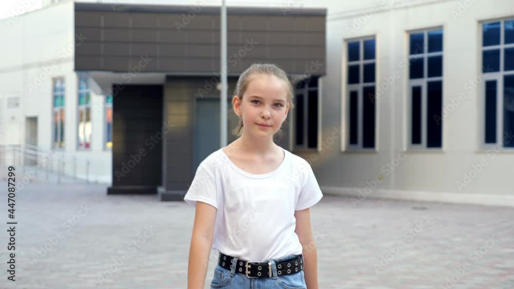 Young lady walks along street. Blonde teenage girl in white t-shirt and blue denim jeans steps on pavement against large city building close view Young lady walks along street. Blonde teenage girl in white t-shirt and blue denim jeans steps on pavement against large city building close view