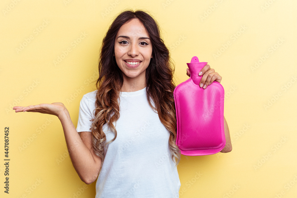 Young mixed race woman holding a hot bag isolated on yellow background showing a copy space on a palm and holding another hand on waist. Young mixed race woman holding a hot bag isolated on yellow background showing a copy space on a palm and holding another hand on waist.