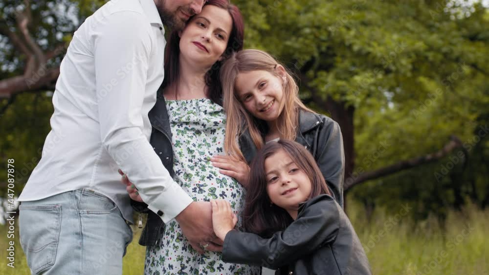 Caucasian family of four standing in strong hugs at green summer garden. Father, mother and two daughters spending weekends on fresh air. Caucasian family of four hugging at green summer garden Caucasian family of four standing in strong hugs at green summer garden. Father, mother and two daughters spending weekends on fresh air. Caucasian family of four hugging at green summer garden