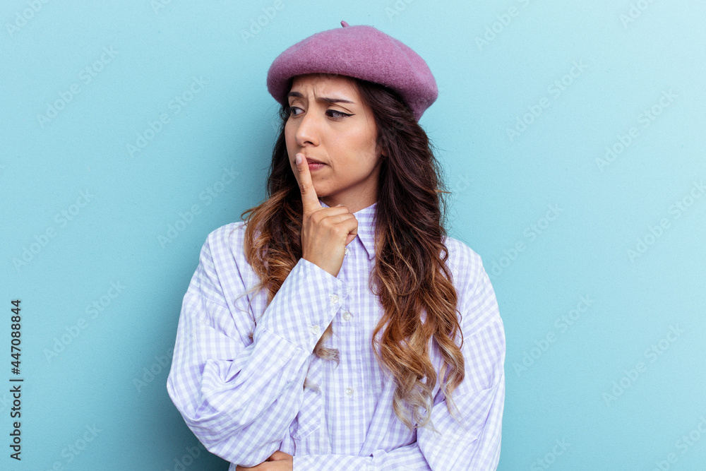 Young mexican woman isolated on blue background looking sideways with doubtful and skeptical expression.
