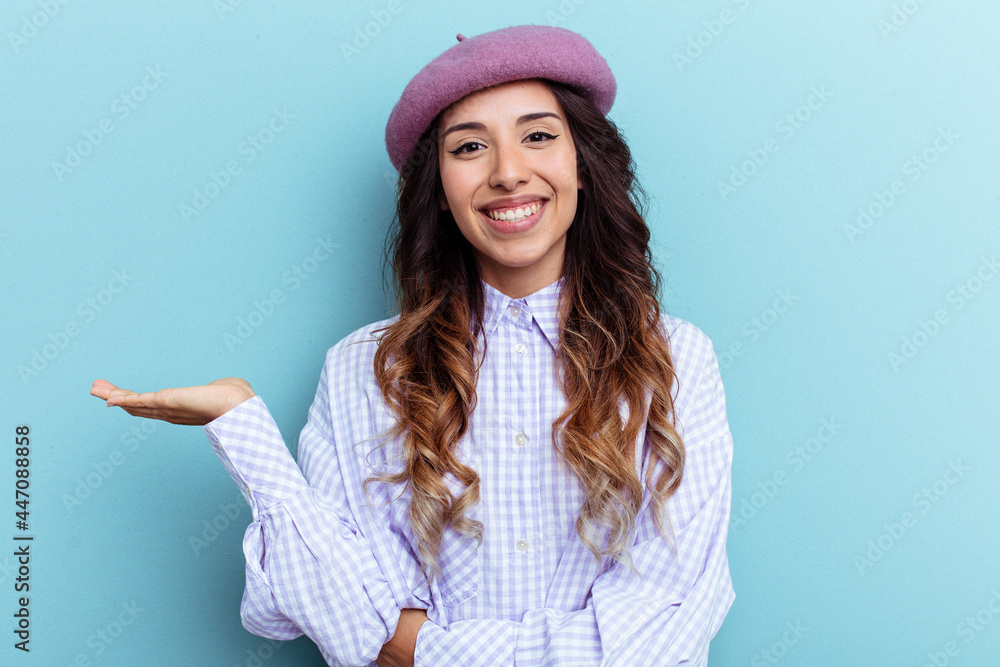 Young mexican woman isolated on blue background showing a copy space on a palm and holding another hand on waist. Young mexican woman isolated on blue background showing a copy space on a palm and holding another hand on waist.