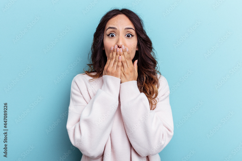 Young mexican woman isolated on blue background shocked covering mouth with hands. Young mexican woman isolated on blue background shocked covering mouth with hands.