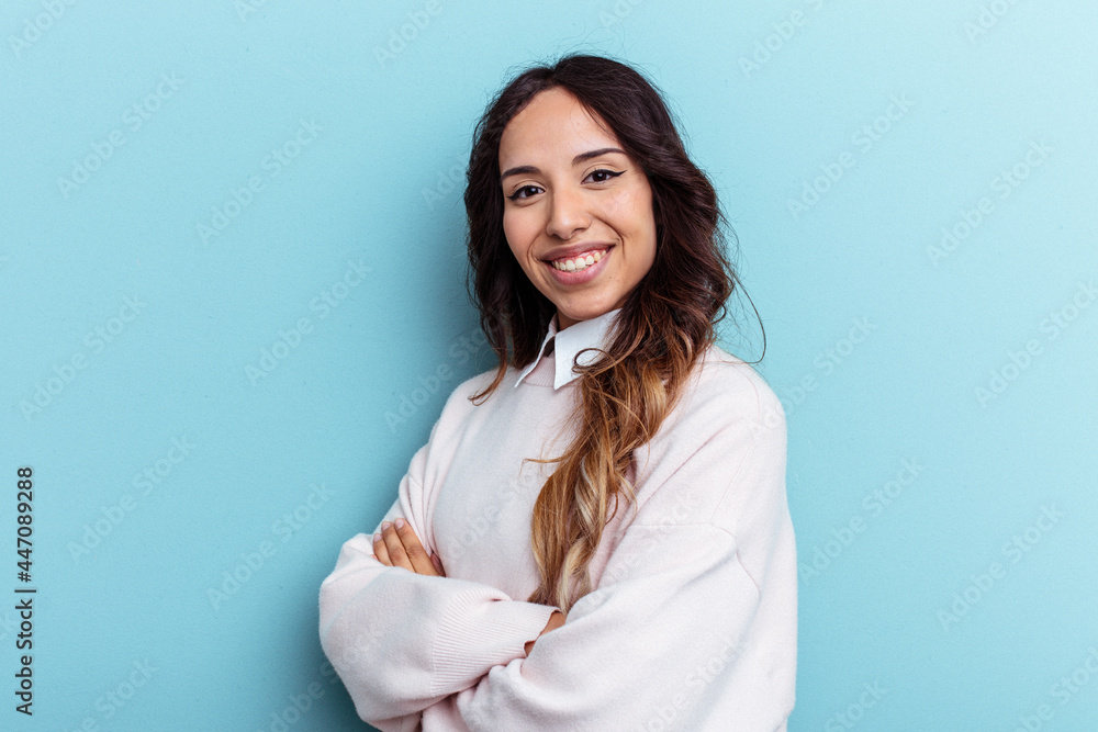 Young mexican woman isolated on blue background who feels confident, crossing arms with determination. Young mexican woman isolated on blue background who feels confident, crossing arms with determination.