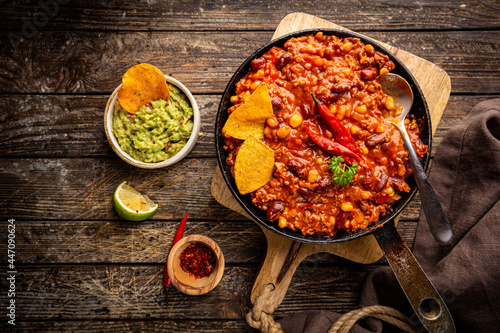 Mexican hot chili con carne in a pan with tortilla chips on dark background, top view