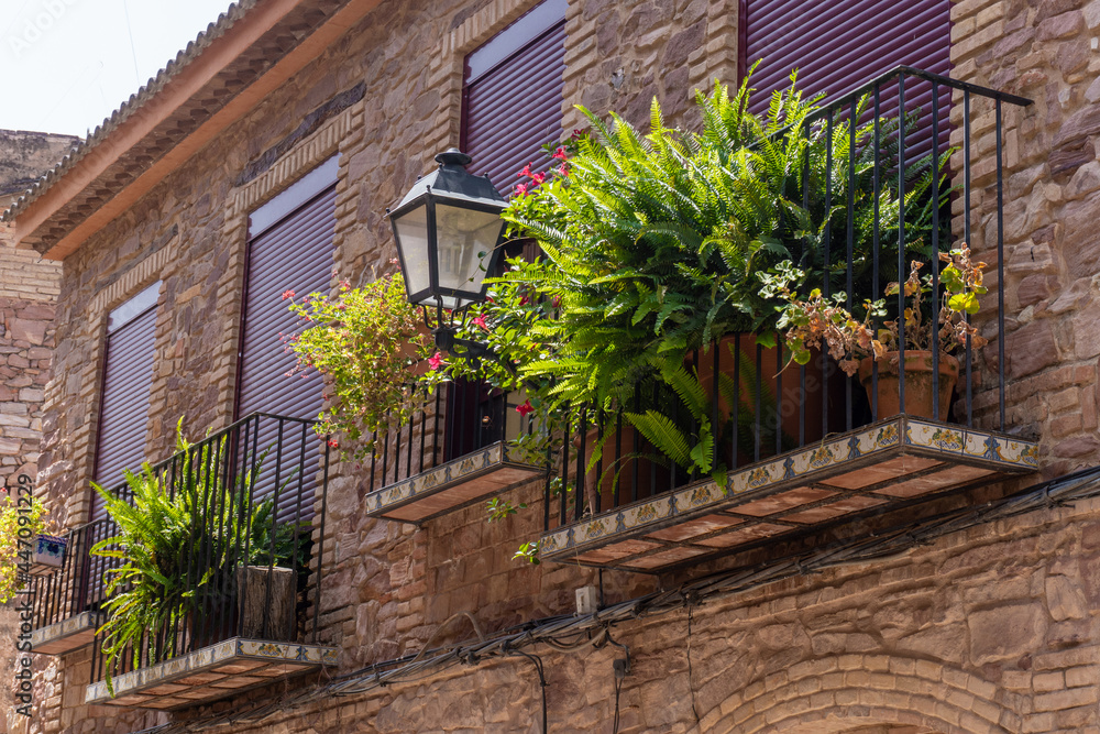 Plant-adorned balconies in a stone-built house, with a black lamppost in the middle of the façade.