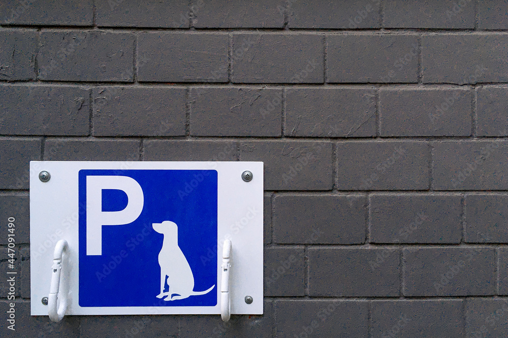 Designated dog parking sign on blue plate. Place for bind dogs waiting for owners outside, with rings for attaching leash, on public place area or shop. Copy space. Close-up. Designated dog parking sign on blue plate. Place for bind dogs waiting for owners outside, with rings for attaching leash, on public place area or shop. Copy space. Close-up.