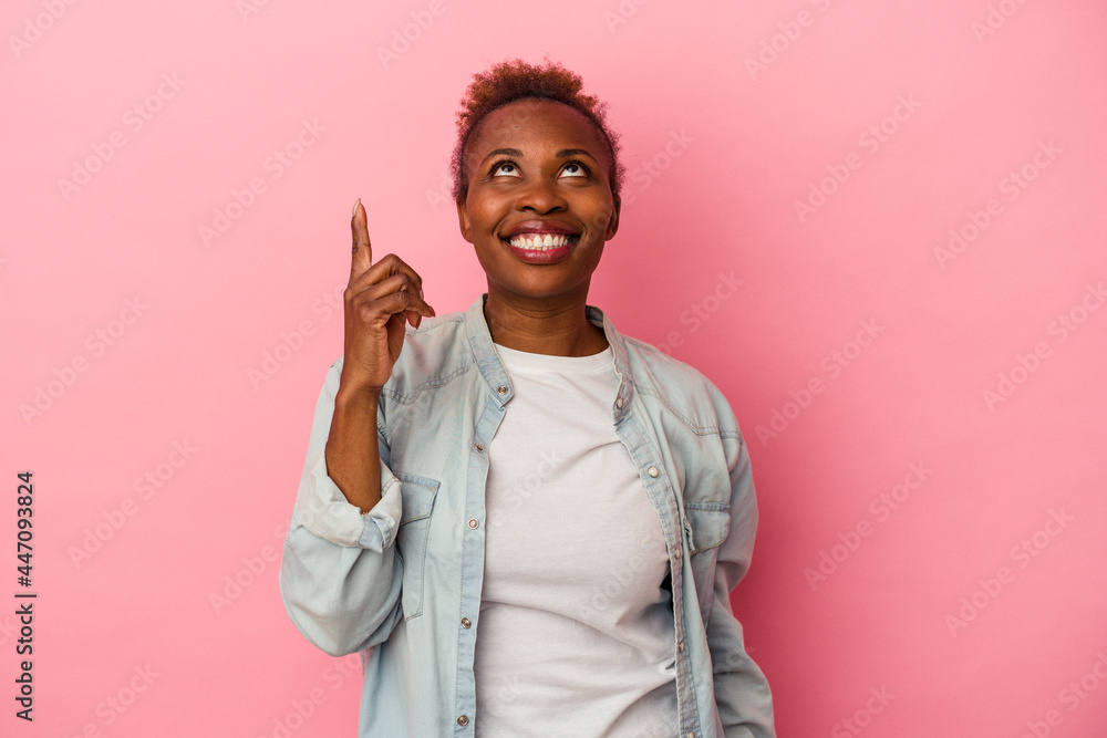 Young african american woman isolated on pink background indicates with both fore fingers up showing a blank space. Young african american woman isolated on pink background indicates with both fore fingers up showing a blank space.