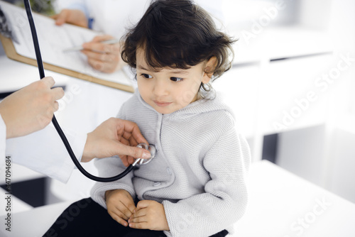 Woman-doctor examining a child patient by stethoscope. Cute arab toddler at physician appointment. Medicine concept
