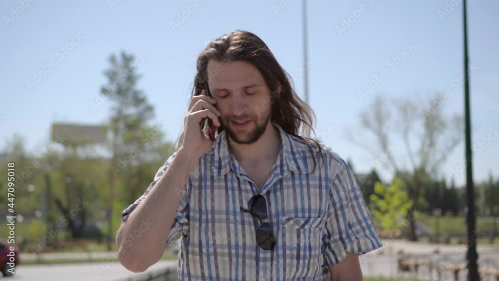 Front view portrait of smiling long haired man talking on the phone walking in the street. Concept of people and emotions. Front view portrait of smiling long haired man talking on the phone walking in the street. Concept of people and emotions.