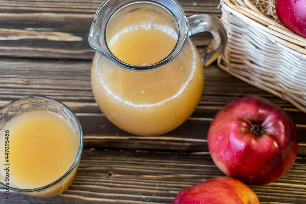 Red apples in a basket and apple juice in a jug on a wooden table Red apples in a basket and apple juice in a jug on a wooden table