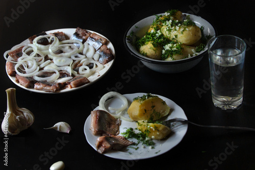 Salted herring fish, cut, with boiled potatoes, herbs and garlic on a dark background.