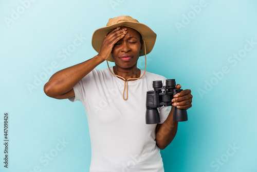 Young african american woman holding binoculars isolated on blue background being shocked, she has remembered important meeting.