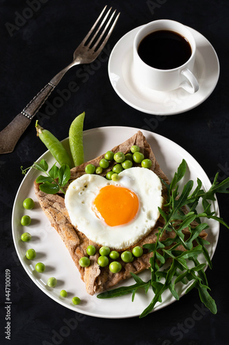 Galette bretonne with egg, arugula and green peas on a black background. Coffee in a white cup.
