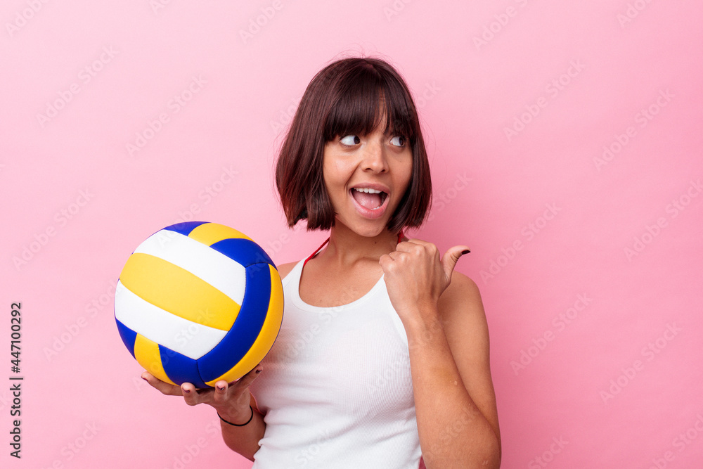 Young mixed race woman playing volleyball isolated on pink background points with thumb finger away, laughing and carefree. Young mixed race woman playing volleyball isolated on pink background points with thumb finger away, laughing and carefree.