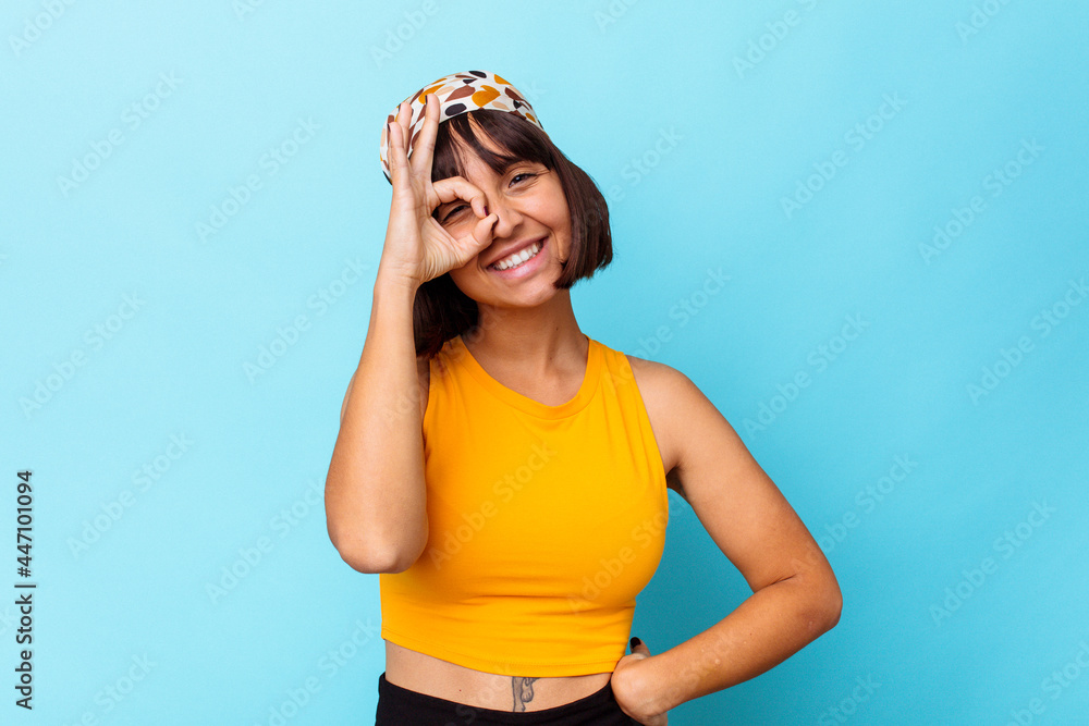 Young mixed race woman isolated on blue background excited keeping ok gesture on eye.