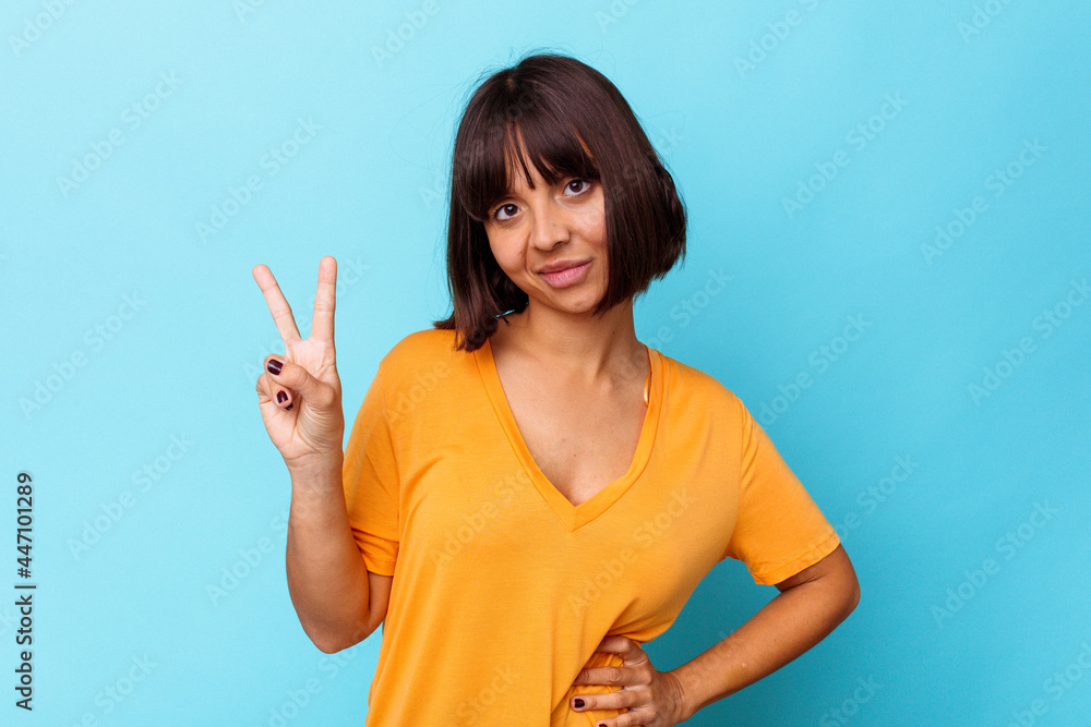 Young mixed race woman isolated on blue background joyful and carefree showing a peace symbol with fingers. Young mixed race woman isolated on blue background joyful and carefree showing a peace symbol with fingers.