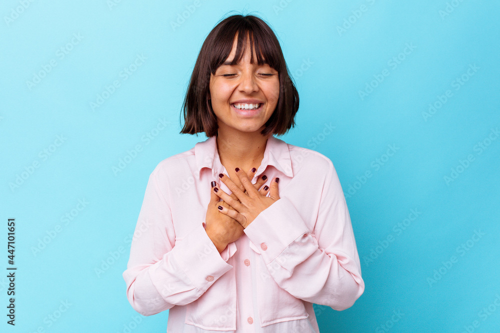 Young mixed race woman isolated on blue background laughs out loudly keeping hand on chest. Young mixed race woman isolated on blue background laughs out loudly keeping hand on chest.