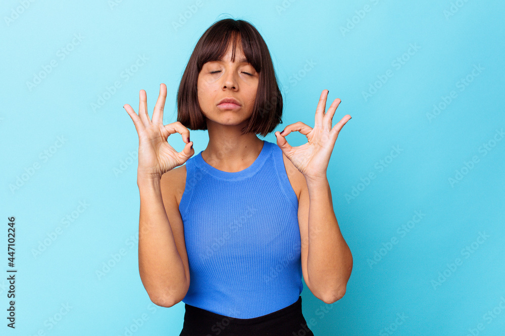 Young mixed race woman isolated on blue background relaxes after hard working day, she is performing yoga.