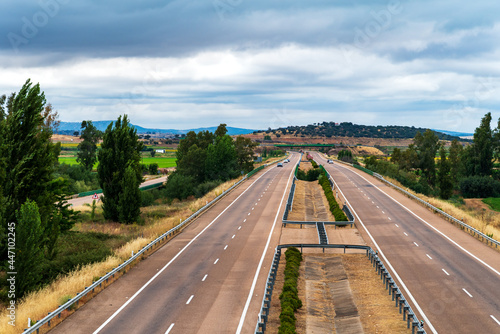 Fotografie Landscape of the Ruta de la Plata highway as it passes through Extremadura, Spain, with trees, low mountains and cloudy skies