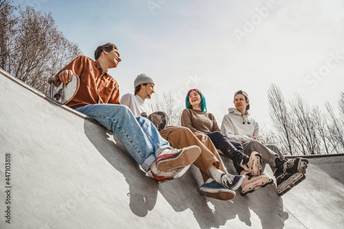 Four cheerful teenagers are happy to meet at the city skatepark, joke and share their impressions after roller skating and skateboarding