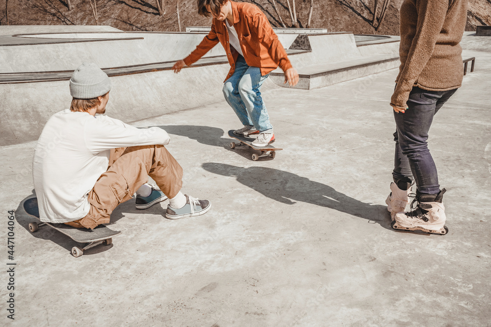 Two boys on skateboards and a girl on roller skates show each other what tricks they can do on the straight surface of a skatepark