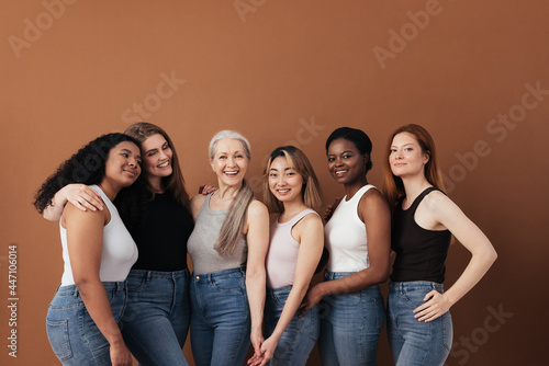 Multi-ethnic group of women of different ages posing against brown background looking at camera