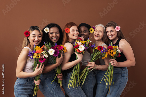 Six smiling women of different ages looking at camera in a studio. Happy diverse females with bouquets and flowers in their hairs standing together. photo