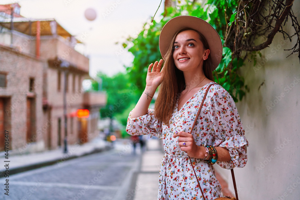 Portrait of young happy smiling cute beautiful brunette traveler girl with long hair wearing hat walking alone around the city at sunny summer day