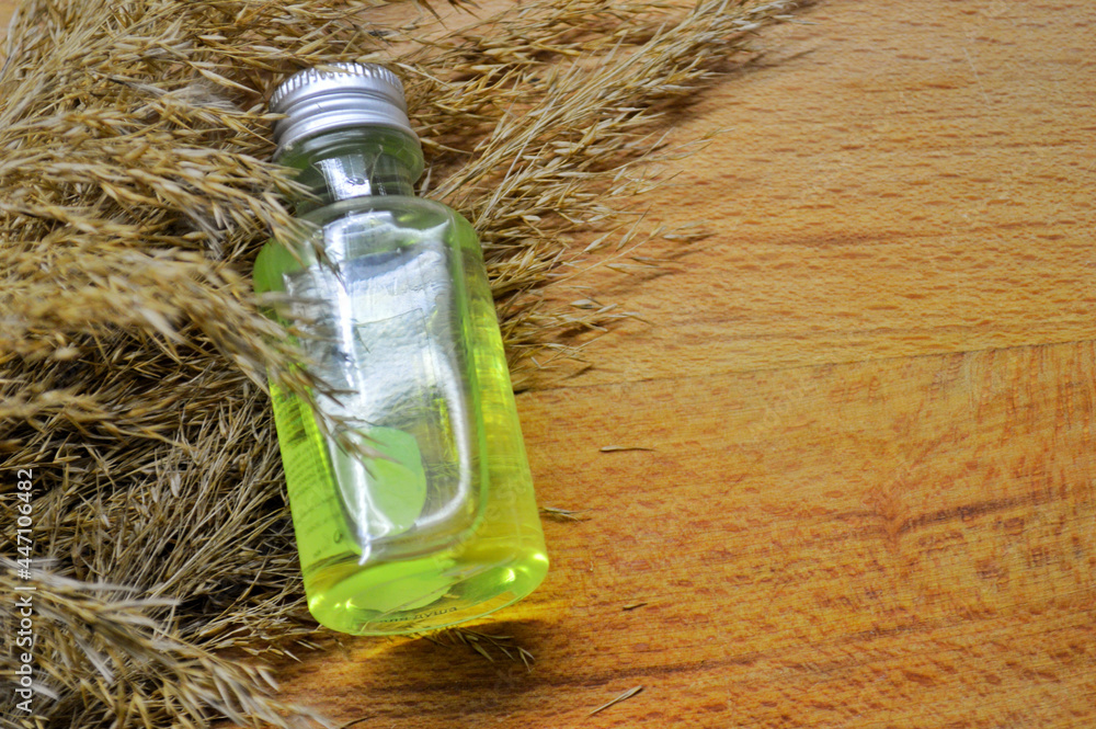 Obraz premium Glass bottle with green gel lies on fluffy dry grass on wooden background