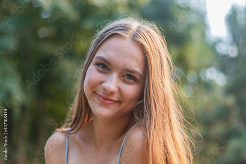 young girl 16 years old, charming brunette with long hair, open smile, against the background of the park, female portrait of a teenager close-up