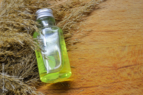 Glass bottle with green gel lies on fluffy dry grass on wooden background