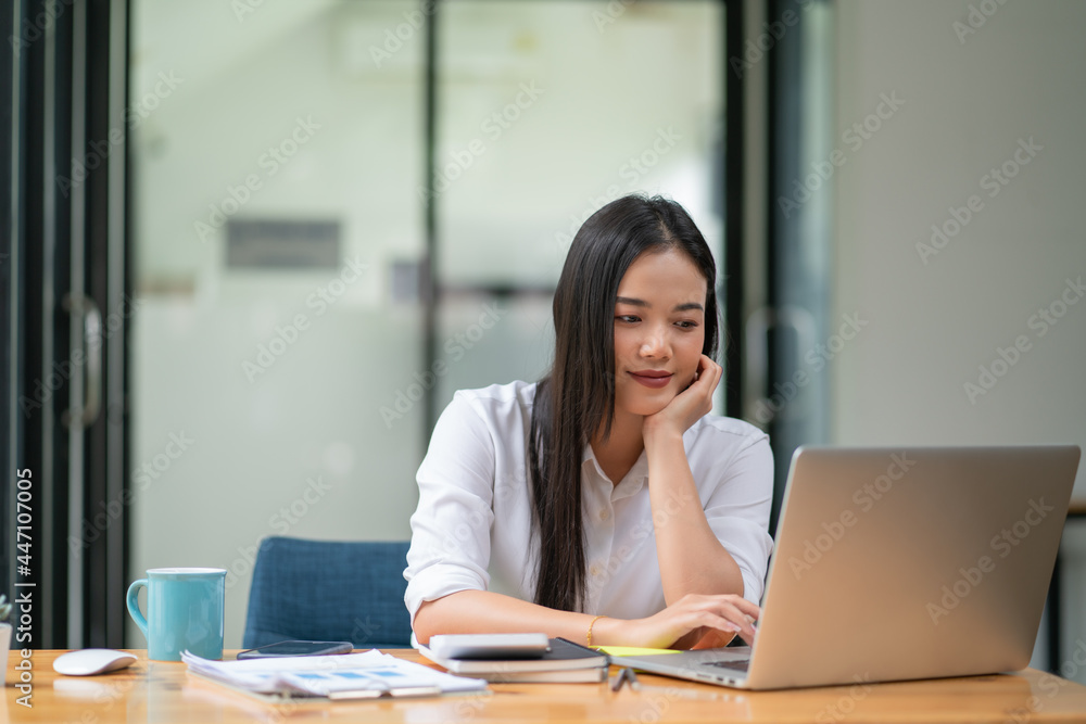 A businesswoman puts her hand on her chin while using a laptop. A businesswoman puts her hand on her chin while using a laptop.