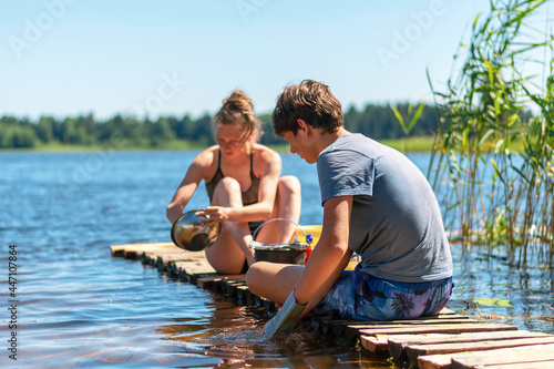 Fotografie A young girl and a boy are washing dishes on a wooden bridge by the lake