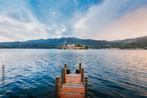 Orta San Giulio / Italy - June 2021: The island of San Giulio with a wooden jetty in the foreground at sunset