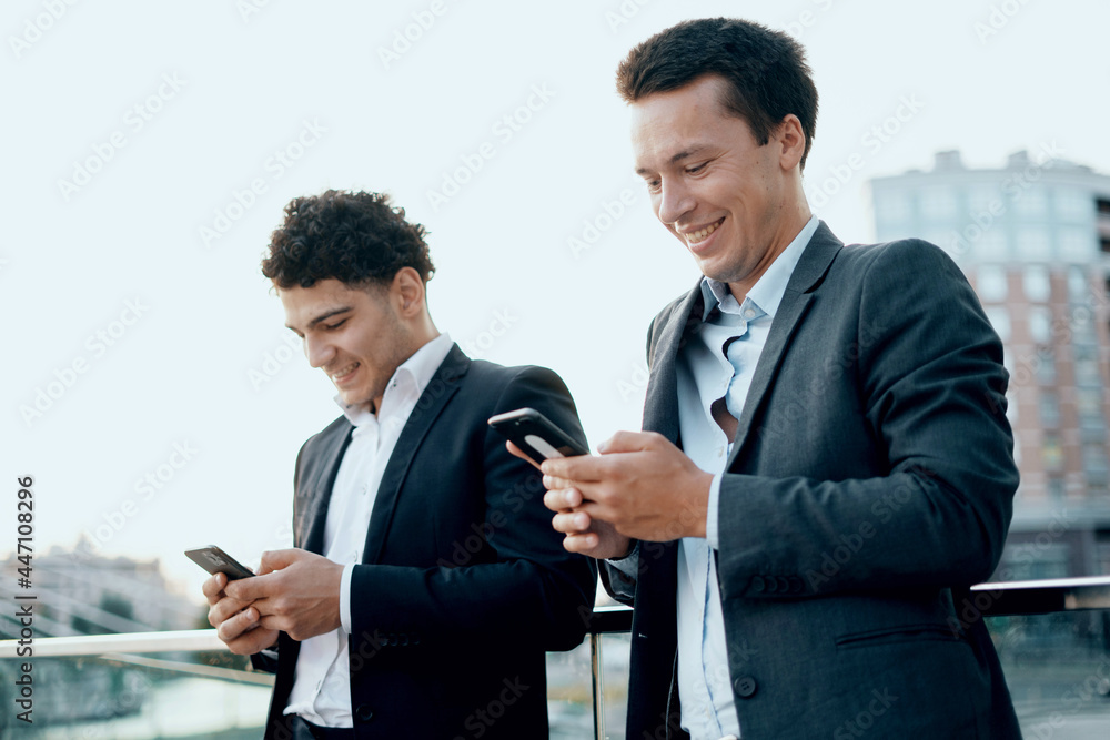 Successful colleagues work together on a social network. Businessmen young people work near the office in business suits holding gadgets in their hands. They are discussing a new startup project. Successful colleagues work together on a social network. Businessmen young people work near the office in business suits holding gadgets in their hands. They are discussing a new startup project.