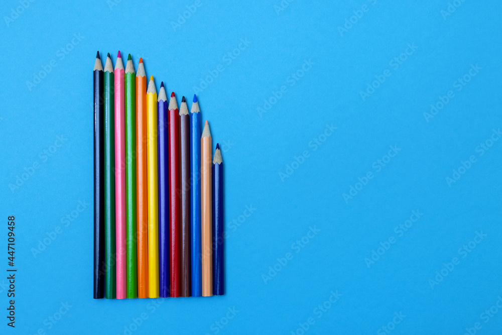 Obraz premium Colored wooden pencils on a blue paper background. Vertically upwards, place for text about school or drawing lessons.