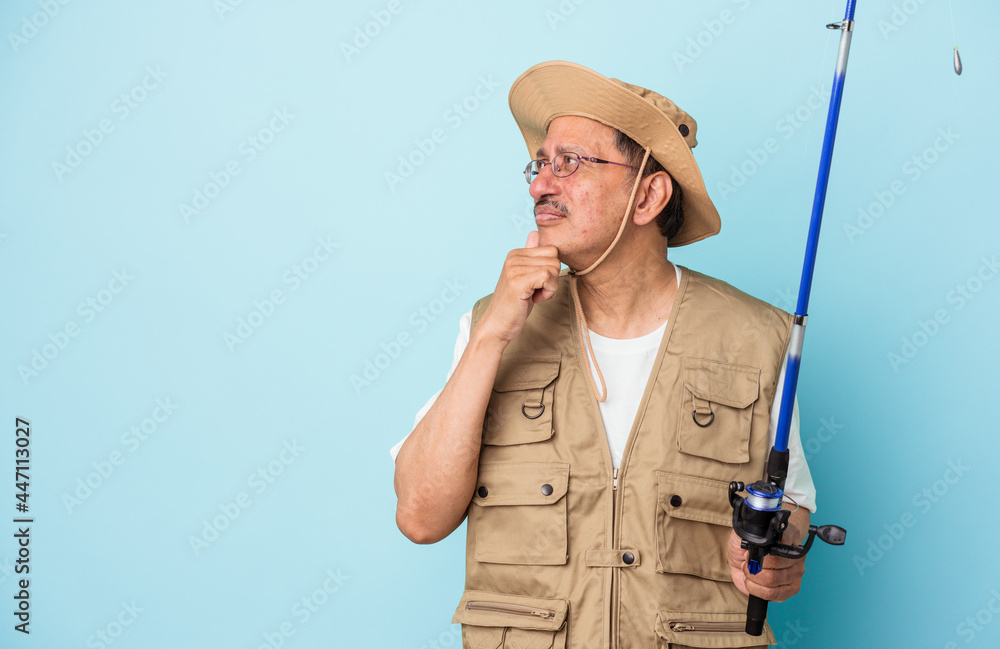 Senior indian fisherman holding rod isolated on blue background looking sideways with doubtful and skeptical expression. Senior indian fisherman holding rod isolated on blue background looking sideways with doubtful and skeptical expression.