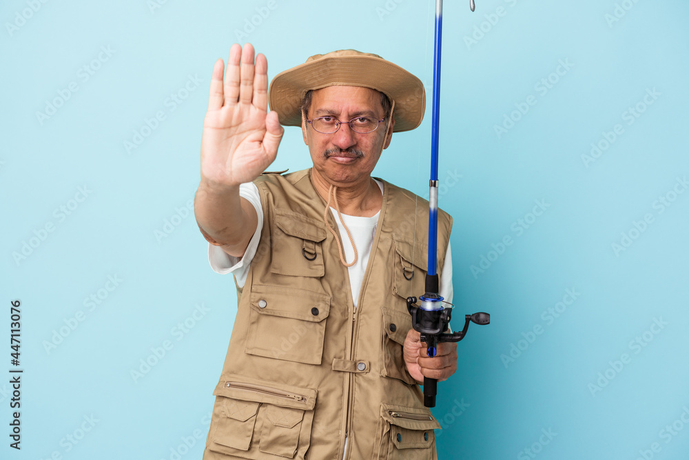 Senior indian fisherman holding rod isolated on blue background standing with outstretched hand showing stop sign, preventing you. Senior indian fisherman holding rod isolated on blue background standing with outstretched hand showing stop sign, preventing you.