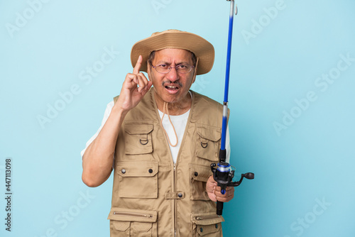 Senior indian fisherman holding rod isolated on blue background showing a disappointment gesture with forefinger.