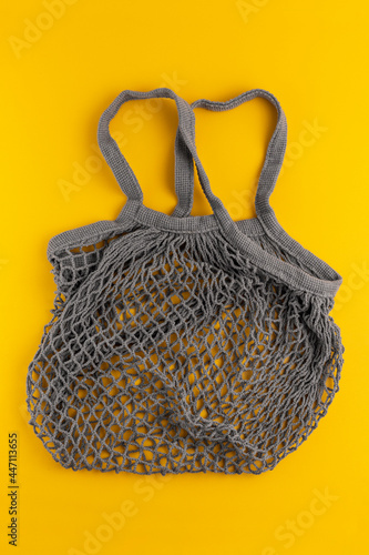 Gray string shopping bag, or net bag, or mesh bag. Top view. On a yellow background.